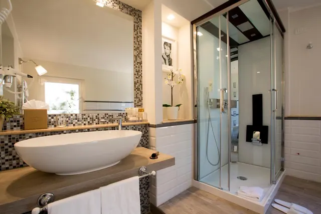 A bathroom with an oval vessel sink on a wooden counter, a mosaic-tiled wall, and a glass-enclosed walk-in shower.