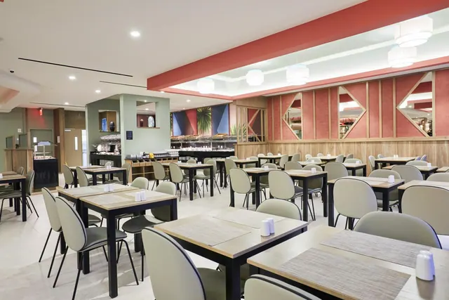A large dining room with rows of grey chairs and tables, with a buffet counter visible in the background.