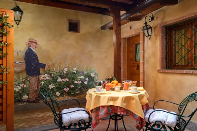 A breakfast table with a yellow cloth, orange juice, fruit and coffee cups sits on a tiled terrace beside a wall mural of a man watering flowers.