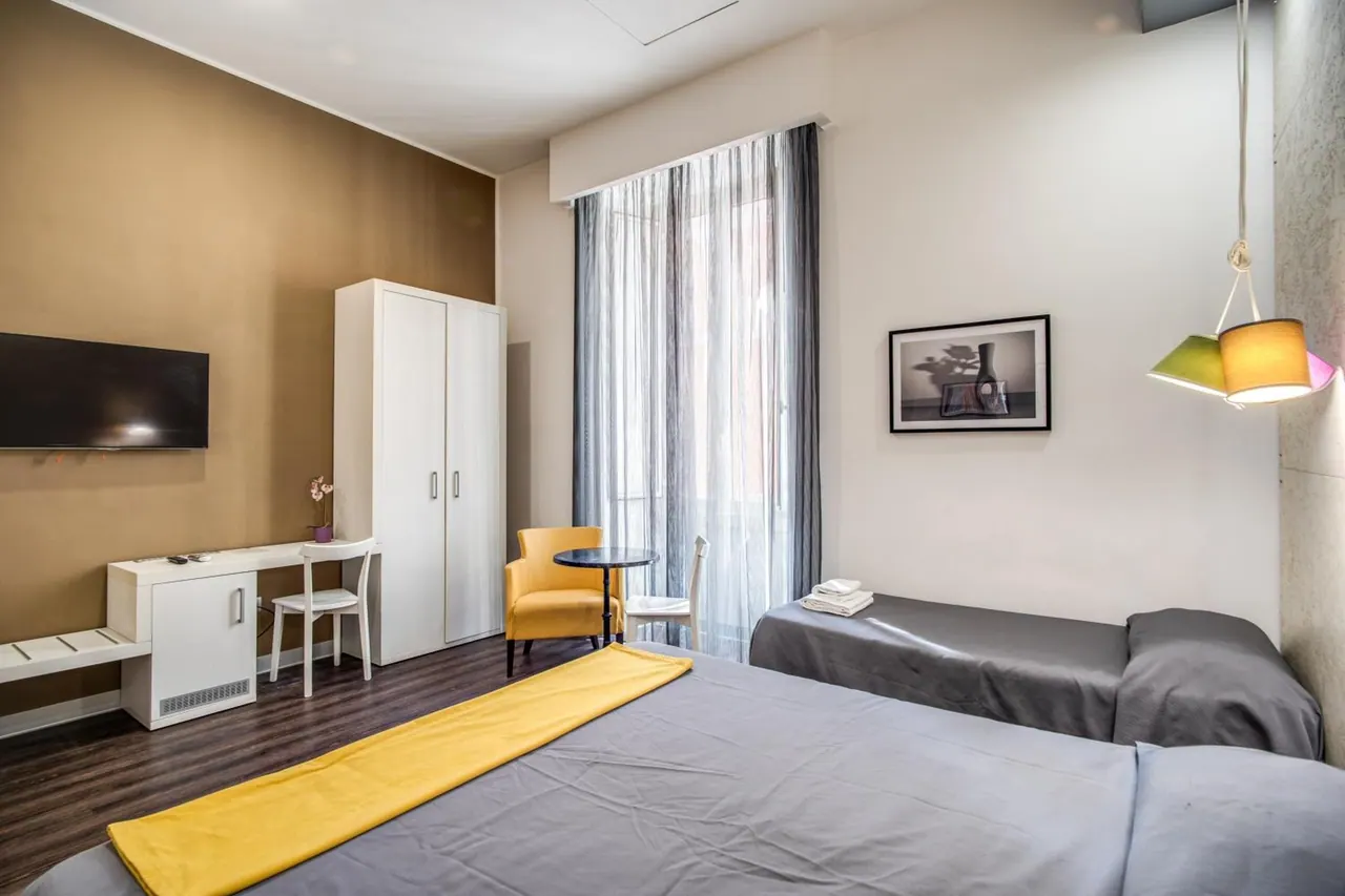 A hotel room with a double bed, a single bed, a yellow armchair, a desk, a wardrobe and a wall-mounted television.
