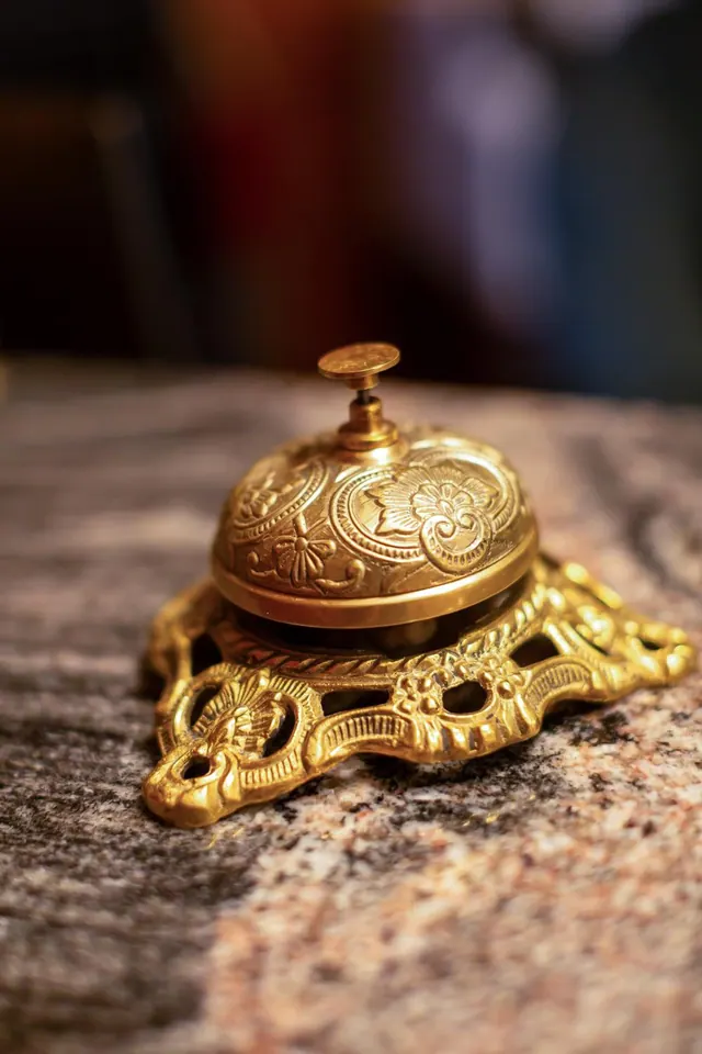 A polished brass service bell with embossed floral patterns sits on a granite surface.