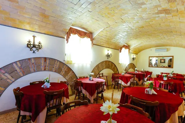 A dining room with a vaulted brick ceiling, arched wall recesses, and round tables with red tablecloths and wooden chairs.