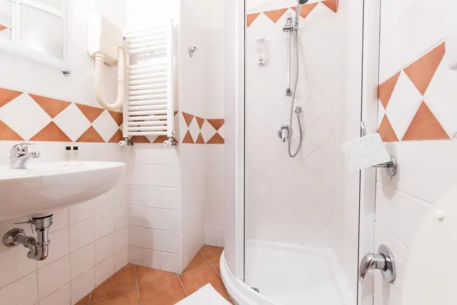 A small bathroom with a wall-mounted sink, a glass-door shower cubicle, a heated towel rail and terracotta diamond-patterned wall tiles.