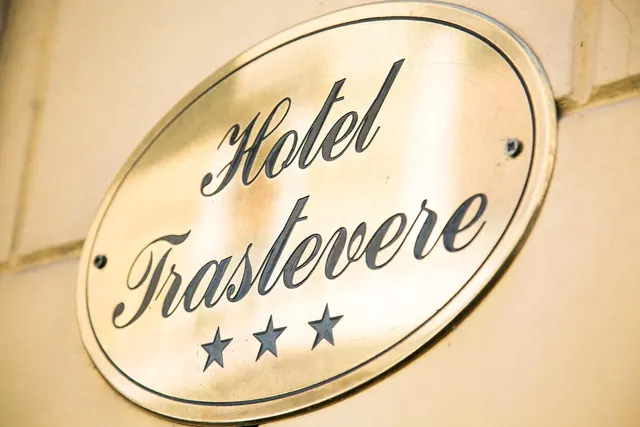 A polished brass oval plaque reading Hotel Trastevere, with three stars, is mounted on a cream wall.