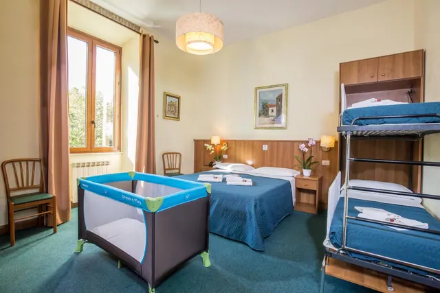 A hotel bedroom with a double bed, a bunk bed, a travel cot and a window looking out onto trees.