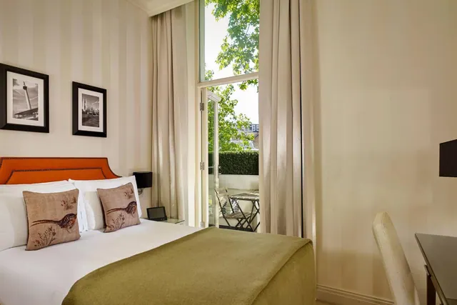 A bedroom with a double bed, orange headboard, striped walls, and French doors opening onto a small balcony with folding chairs and a table.