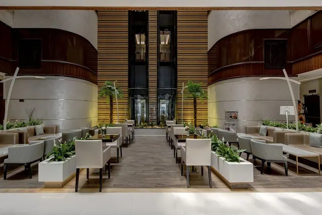 A symmetrical lobby seating area with armchairs, low tables, potted plants and a central bank of lifts.