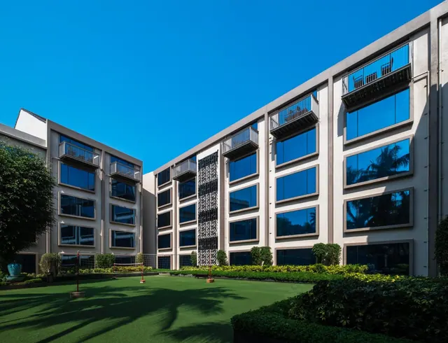 A modern hotel building surrounds a landscaped courtyard with a lawn and volleyball net.