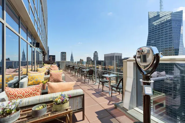 A rooftop terrace with lounge seating, bistro tables and a coin-operated viewing telescope overlooks city skyscrapers, including the Chrysler Building.