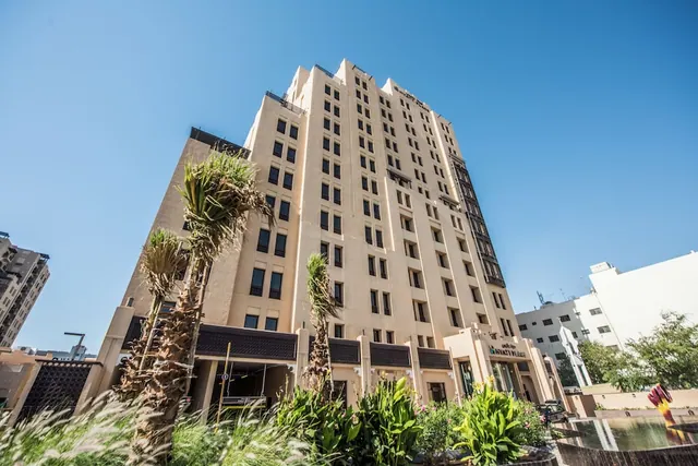A tall beige hotel tower with a Hyatt Place sign at its entrance, with palm trees and plants in front under a clear blue sky.