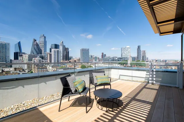 A private balcony with two chairs, a round table and glass railings overlooks a city skyline that includes the Gherkin.
