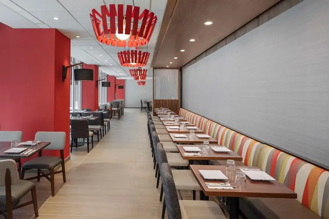 A dining room with red walls, red pendant lights, and a striped banquette with tables set for a meal.
