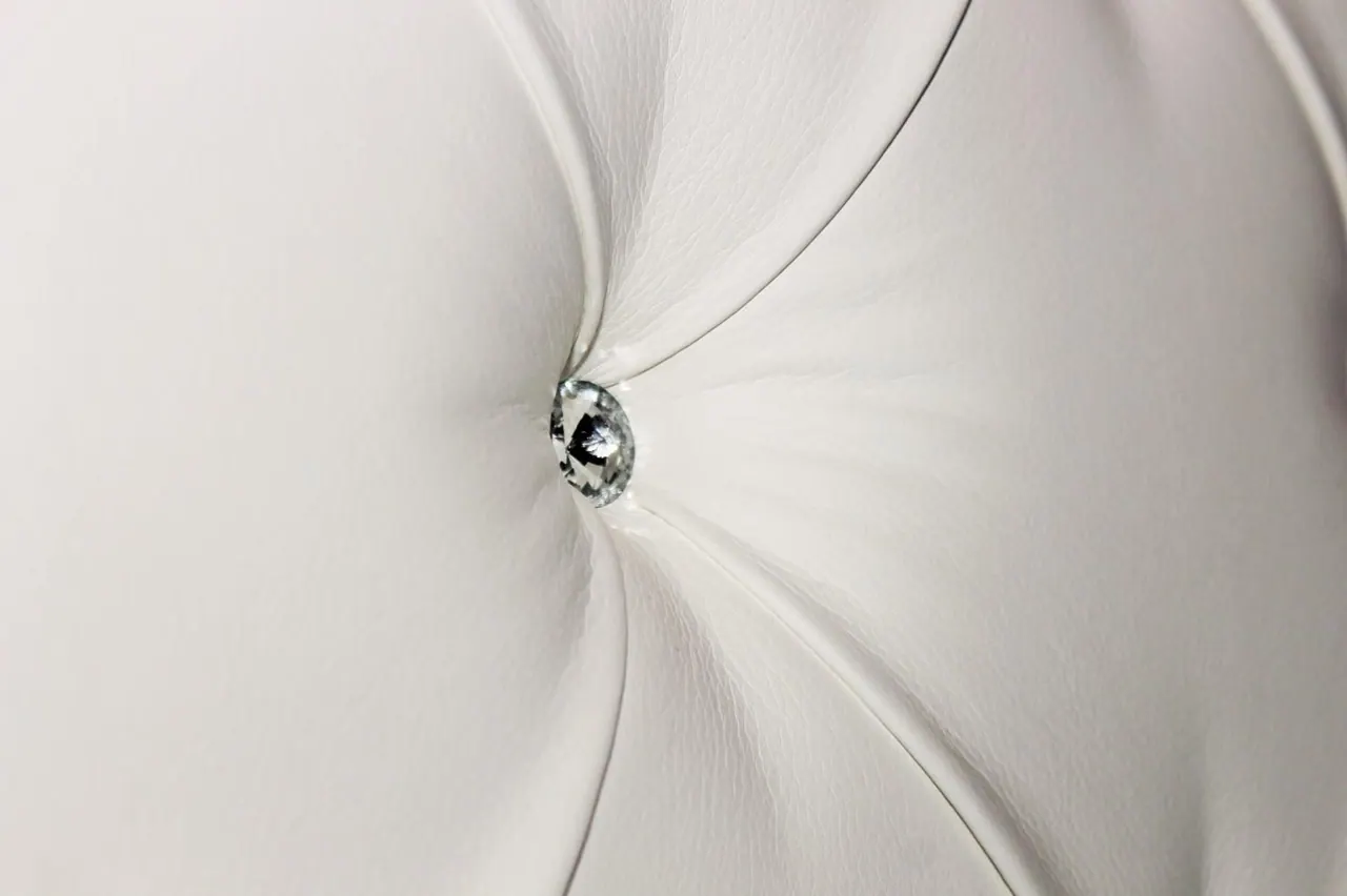 Close-up of a white tufted headboard with a crystal button at its centre.