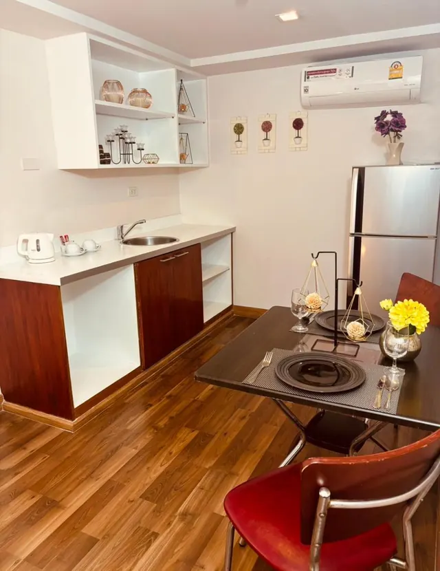 A small room with a kitchenette, a dining table set with plates and glassware, a wall-mounted air conditioner and a stainless steel refrigerator.