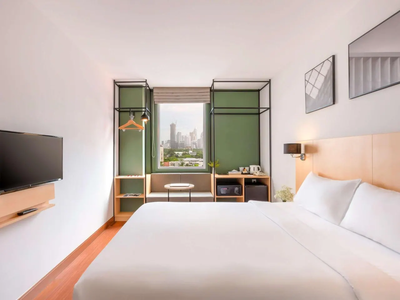 A bedroom with a king bed, a wall-mounted television, and a window looking out over a city skyline.