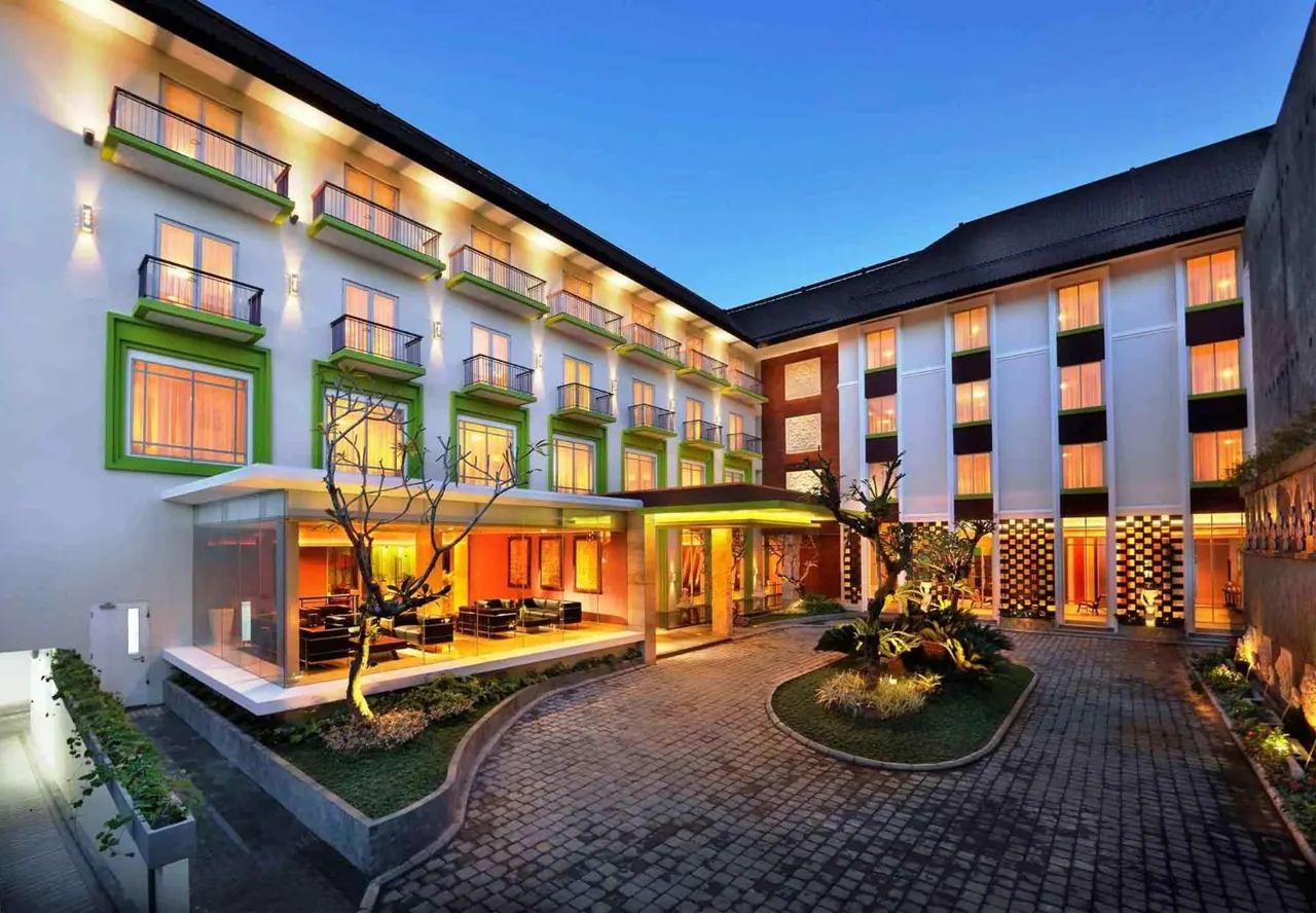 Exterior of a multi-storey hotel building at dusk, with lit balconies, a central courtyard and a cobbled driveway.
