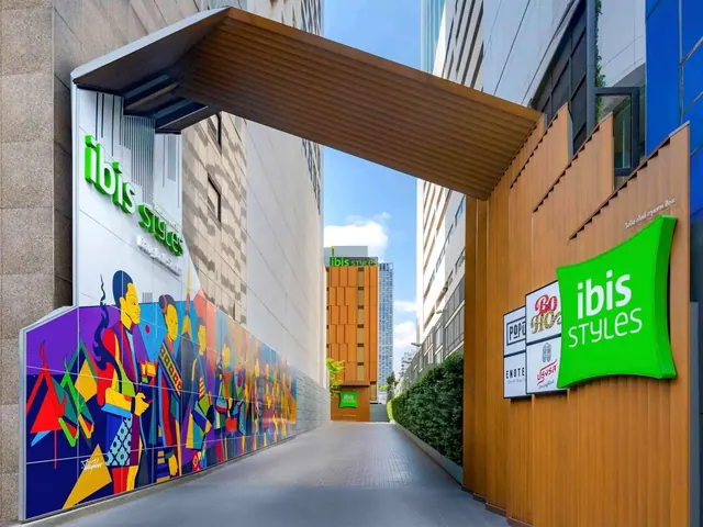 A covered walkway leads past a colorful mural and green ibis Styles signage on the hotel's exterior.