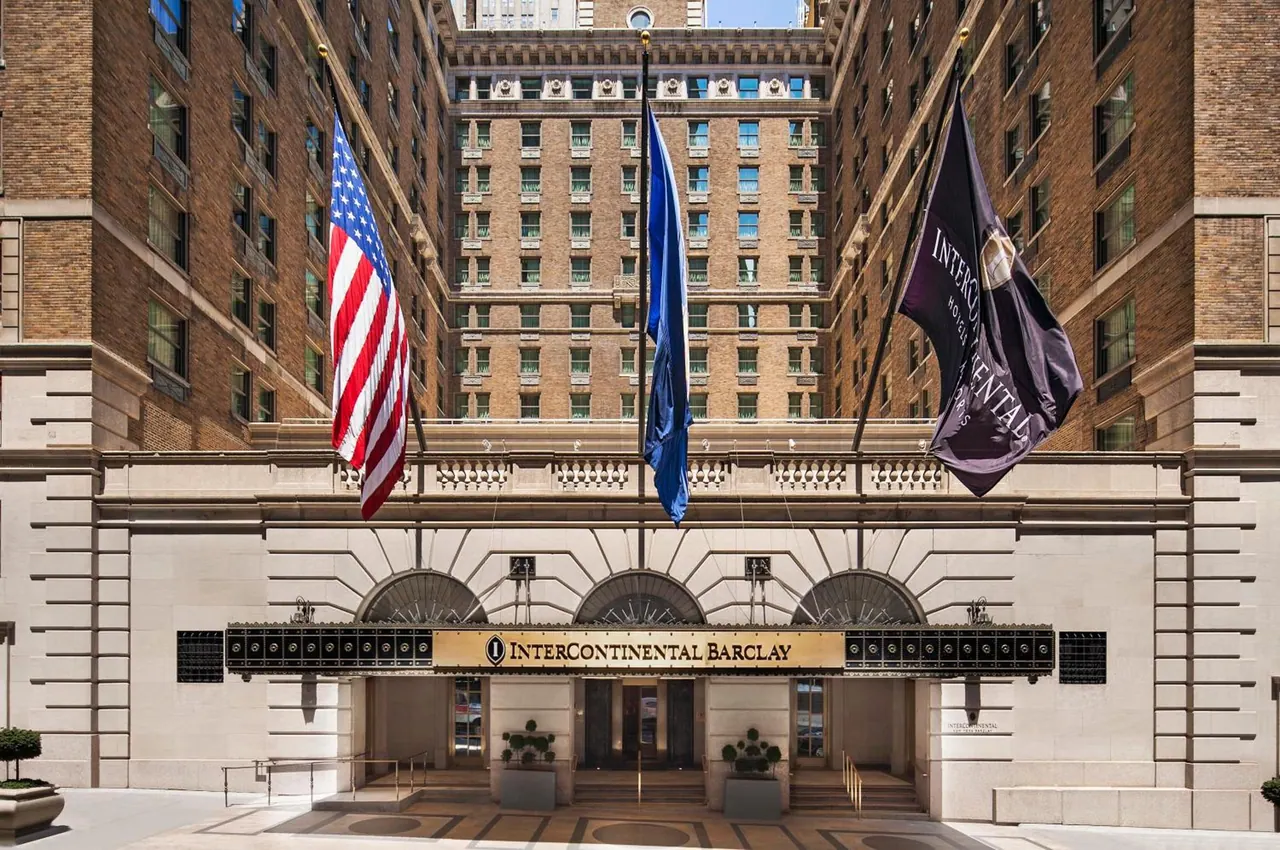 The front facade of the InterContinental Barclay hotel, with an American flag, a blue flag and a purple InterContinental flag on poles above the entrance canopy.