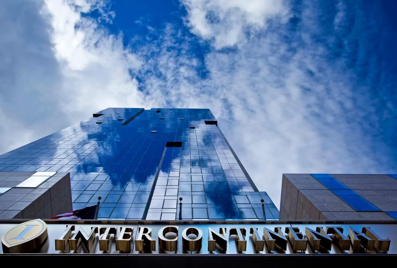 Low-angle view of a blue reflective glass hotel tower under a cloudy sky, with a gold InterContinental sign along the base.