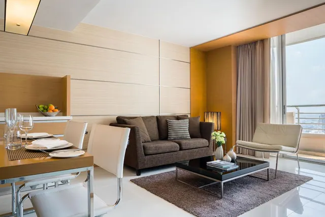A staged living area with a dining table, brown sofa, coffee table and armchair beside a large window with a hazy city view.
