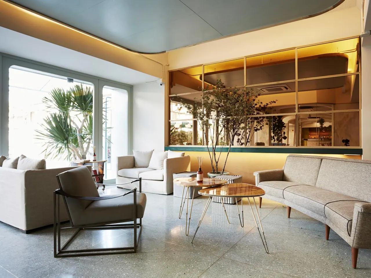 A lounge seating area with grey sofas, armchairs and wooden coffee tables beside large windows and a glass partition.