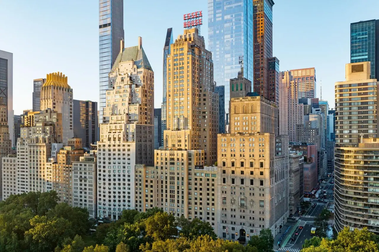 Elevated view of Manhattan high-rise buildings above green treetops, with a red rooftop sign reading Essex House.