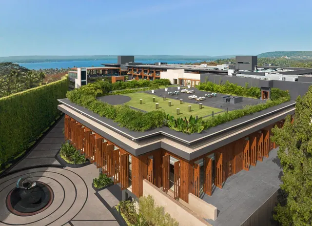 An elevated view shows a modern resort building with landscaped terraces, outdoor seating, and the sea beyond.