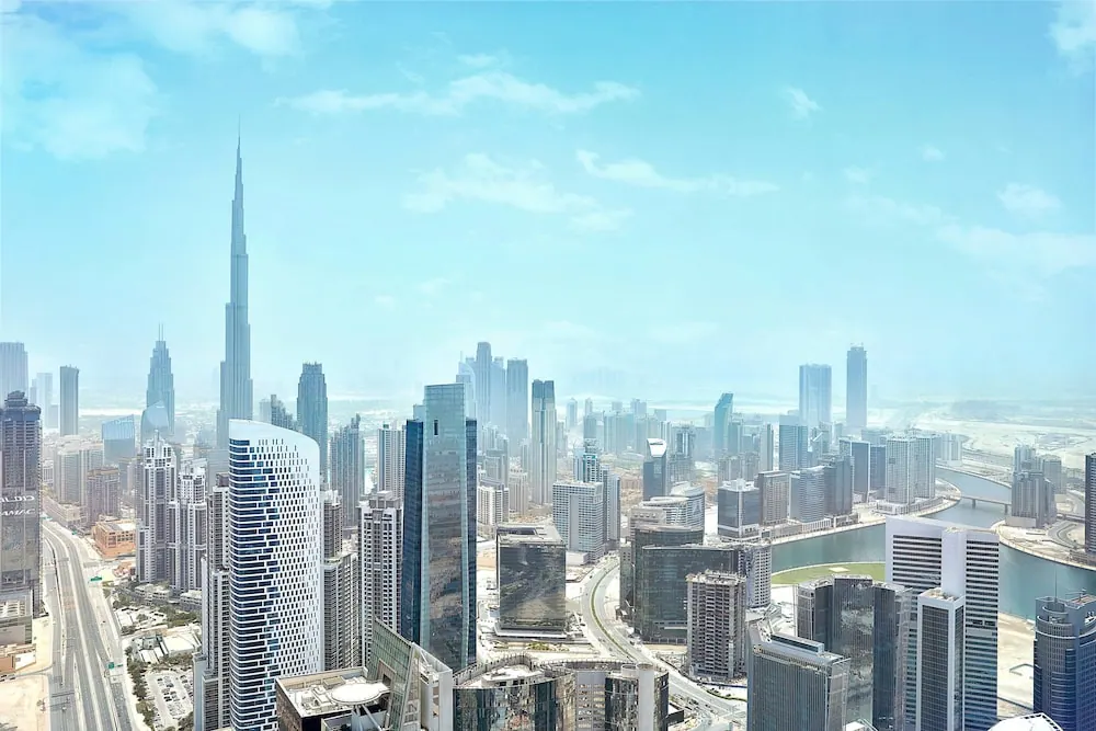Elevated view over a dense city skyline with the Burj Khalifa tower on the left and a canal curving between high-rise buildings on the right.