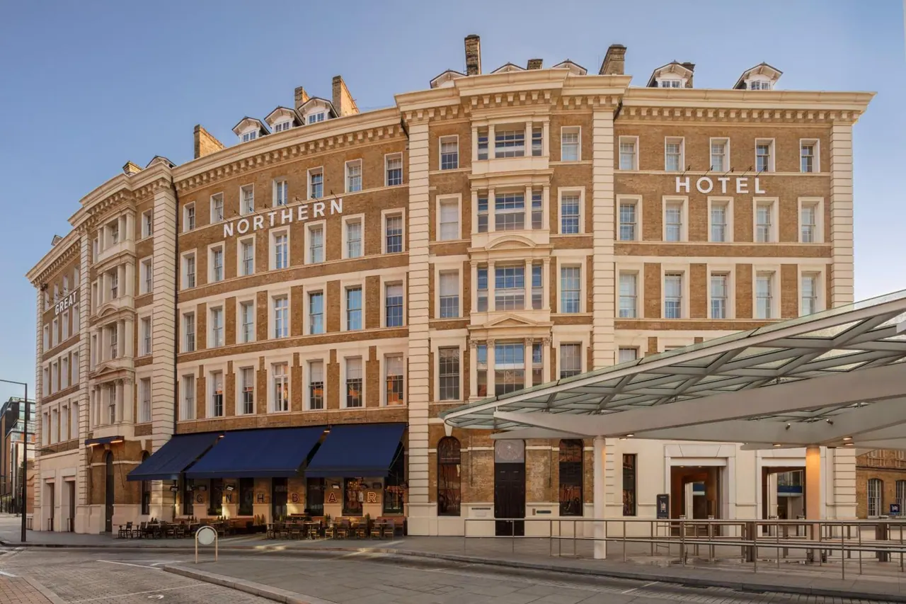The brick facade of a large Victorian-style hotel with Northern and Hotel signage, a glass canopy over the entrance, and outdoor tables under blue awnings at street level.