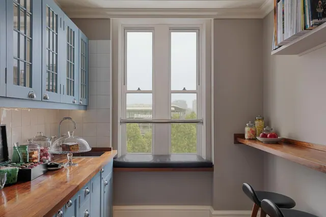 A kitchen with blue glass-fronted cabinets, a wooden worktop and a window looking out over trees, buildings and the St Pancras station sign.