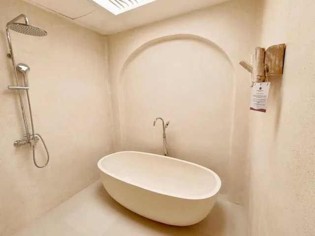 A bathroom with a freestanding oval bathtub, a wall-mounted rain shower with handheld head, an arched wall niche, and a skylight above.