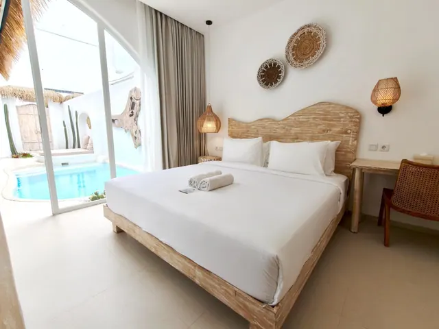 A bedroom with a king bed, wooden headboard and wall-mounted baskets, with sliding glass doors opening onto a private pool.