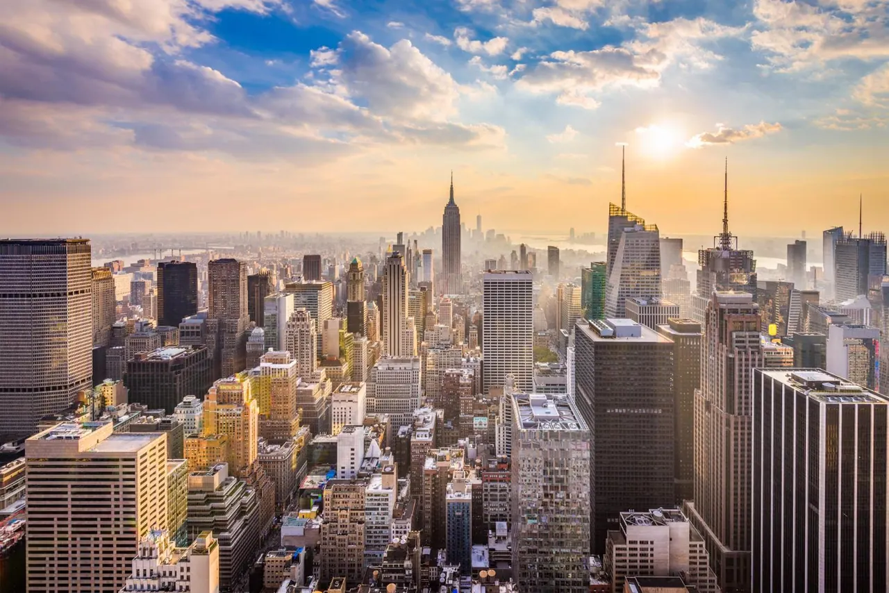 Aerial view of the Manhattan skyline at sunset, with the Empire State Building visible in the distance.