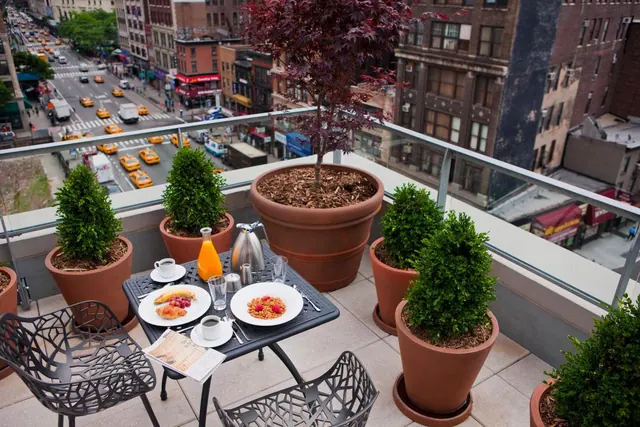 A breakfast table with plates, juice and coffee sits on a rooftop terrace overlooking a busy city street lined with yellow taxis.