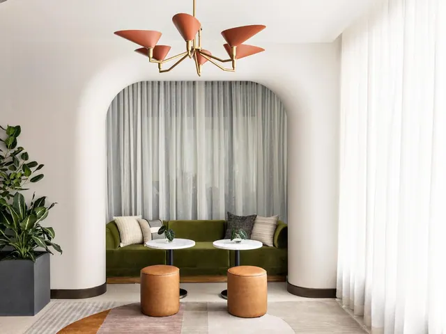 A lounge seating area with a green velvet sofa, leather ottomans, round marble tables, and an orange chandelier in an arched alcove.
