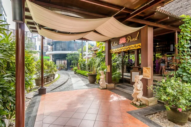 A covered tiled walkway with a fabric canopy leads past stone statues and a sign reading Lotus Pond Cafe, with plants on both sides.
