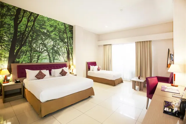 A hotel bedroom with a king bed and a twin bed, a forest mural on the wall, and an armchair and desk near the window.