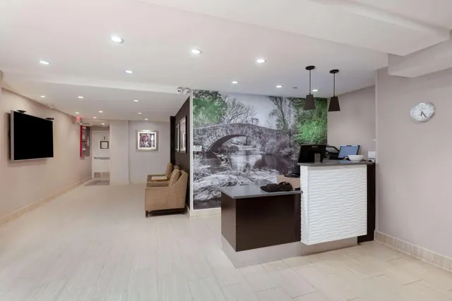 A hotel lobby with a reception desk with a computer monitor, a black-and-white bridge mural on the back wall, a seating area and a wall-mounted television.