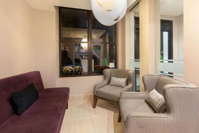 A lobby seating area with a purple sofa, two upholstered armchairs and a window looking out onto a street.