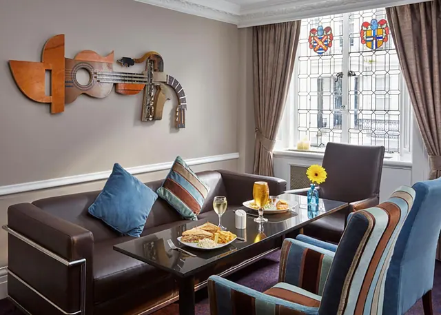 A lounge seating area with a leather sofa, striped armchairs, a glass table with food and drinks, and a stained glass window.