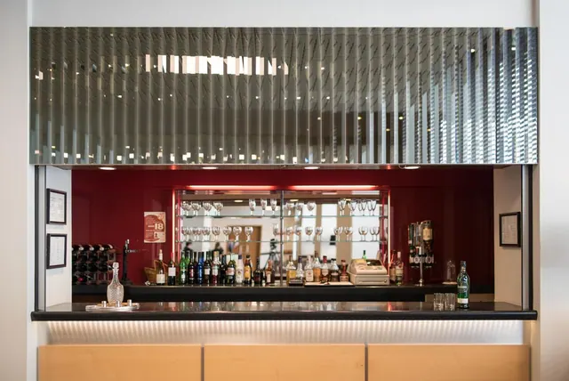 A hotel bar with rows of bottles and wine glasses on shelves against a red wall, with a cash register on the counter.