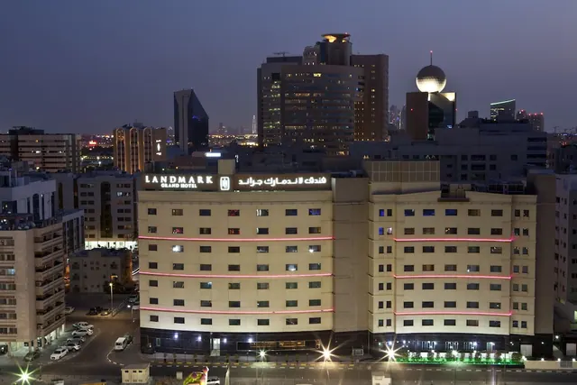 Exterior of the Landmark Grand Hotel, a multi-storey cream building with illuminated signage, photographed at dusk with city towers behind.