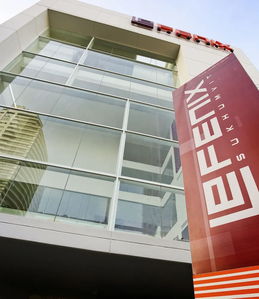 Low-angle view of a glass-fronted building with a red vertical banner and red rooftop lettering against a pale sky.