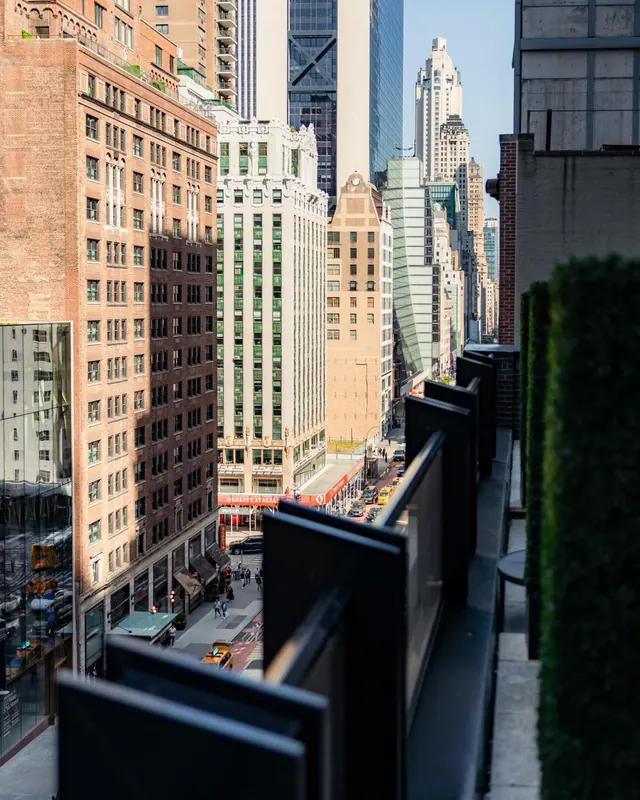 A view from a balcony with black railings looking down a city street lined with tall buildings and yellow taxis.