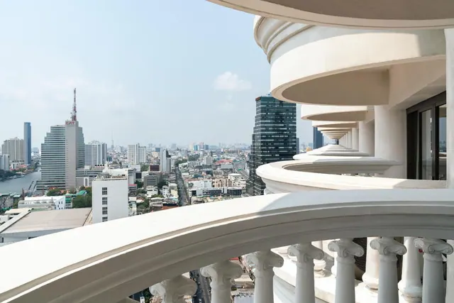 A curved white balcony with classical columns overlooks a dense city skyline and a river on the left.