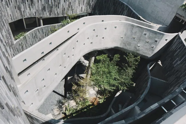 Looking down from above into a courtyard with trees, surrounded by curving concrete walkways and stone-clad walls.