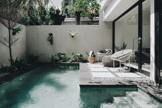 A small walled private pool with stepping stones, white wicker lounge chairs and a large glass sliding door beside it.