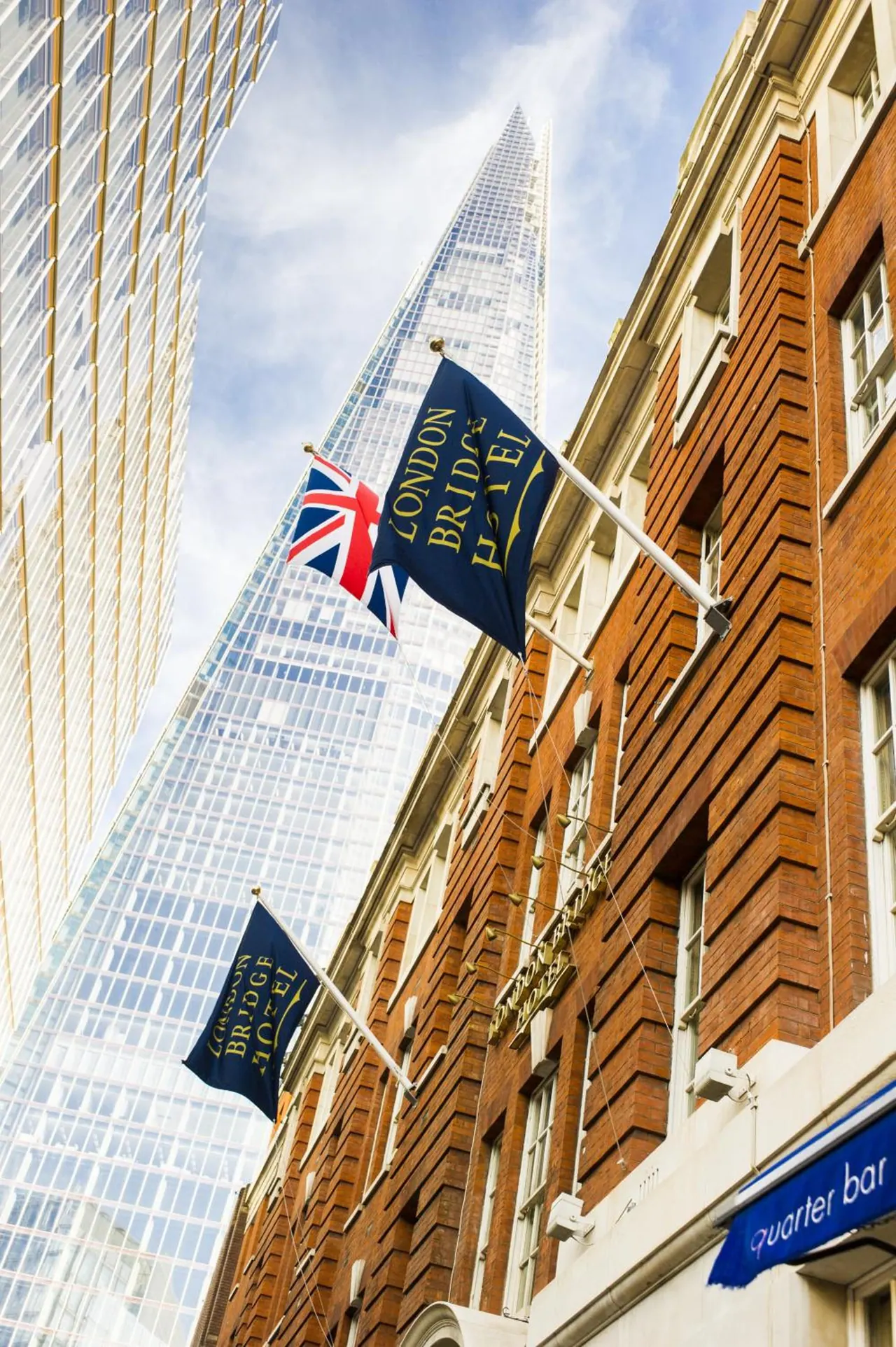 The brick facade of the London Bridge Hotel with navy flags and a Union Jack, with The Shard tower rising behind it.