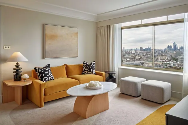 A living area with a mustard velvet sofa, a marble-topped coffee table and a large window looking out over a city skyline.
