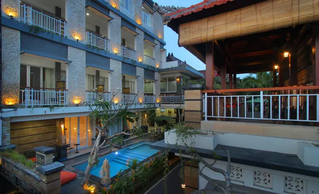 Dusk exterior of a multi-storey hotel with balconies, a small courtyard pool with a statue, and a traditional pavilion with a bamboo blind.